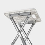 Foldable white stool with metal frame, showing sturdy construction and easy-fold mechanism.