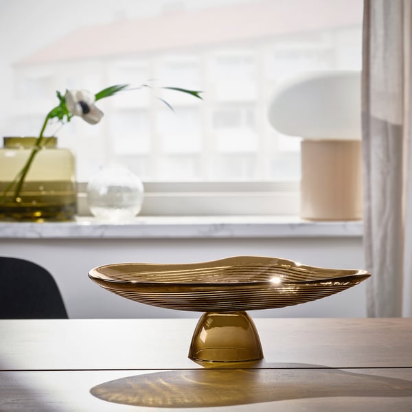 Gold glass bowl inspired by lake ripples sits on table, reflecting light. Decorative or holds items.