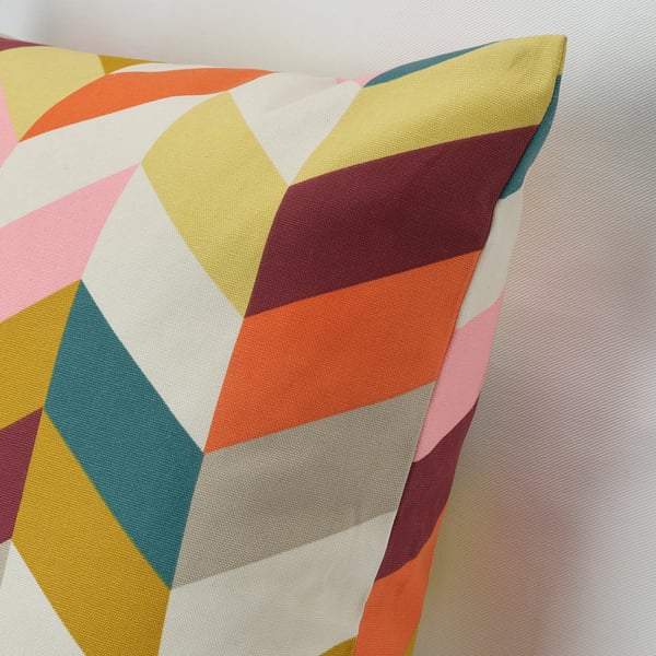 Colorful geometric throw pillow with multiple shades, leaning against a striped background. High-quality cotton and vibrant, interlocking shapes.