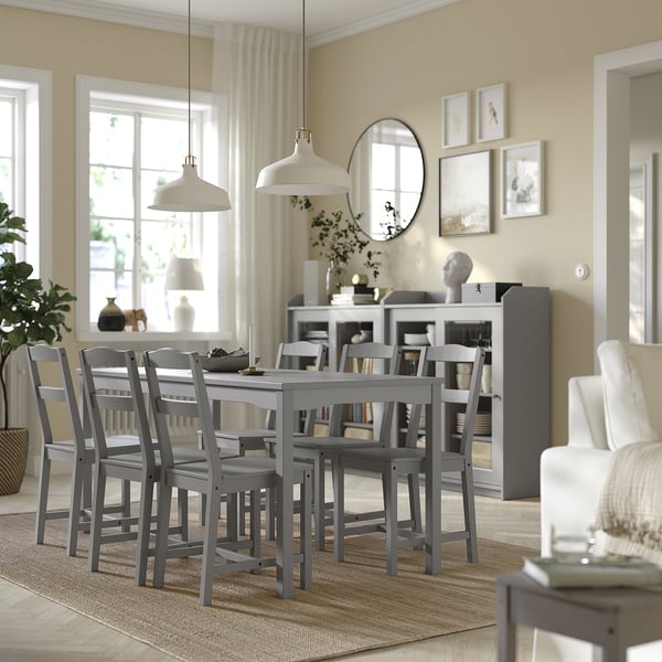 Modern dining area with gray wooden table, chair, rug, white accents, and large windows.