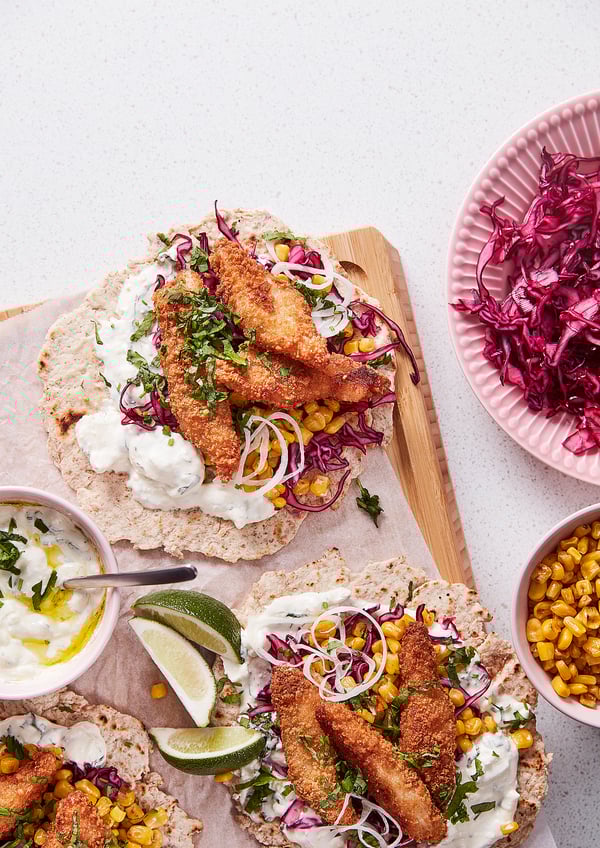 Fish tacos with lime, corn, cabbage, and sour cream on tortillas.