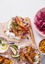 Fish tacos with lime, corn, cabbage, and sour cream on tortillas.
