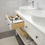 Bathroom vanity with open drawer showing toiletries, including an open shelf for towels. Two sinks on top.
