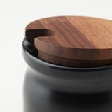 Black ceramic jar with wooden lid. High-quality, close-up view showcasing smooth surface and tight-fitting lid.