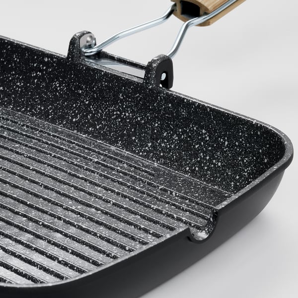 Black grill pan with speckled non-stick coating and wooden handle, ideal for even heat distribution and easy cooking.