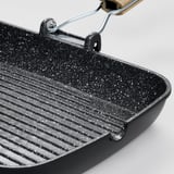 Black grill pan with speckled non-stick coating and wooden handle, ideal for even heat distribution and easy cooking.