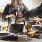 Woman cooks in stylish pan with non-stick coating. Steam vent and comfortable handle visible.
