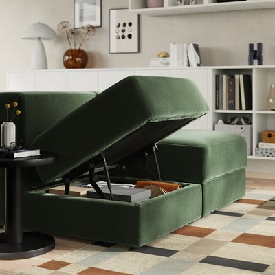 Modern living room with green JÄTTEBO sofa, one section open revealing storage with books and blankets, stylish decor around.