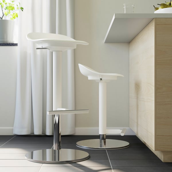 Two modern white barstools with chrome bases and footrests positioned in a minimalist kitchen.