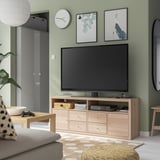Modern living room with KALLAX light oak tv stand. Flat screen tv, gaming controllers, green walls, pillows, and patterned rug.