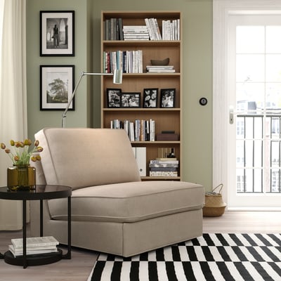 Beige KIVIK sofa, bookshelf, rug, flowers, lamp, city view window.