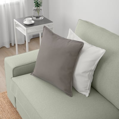 Light-green sofa with gray and white pillows, side table with tea set, and plant vase.