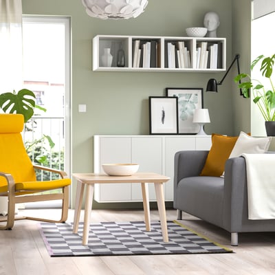 Modern living room with KLASSRUM gray and white checkered rug, yellow chair, gray sofa, wooden coffee table, and green wall.