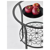 Modern side table with curved steel legs and glass top. Three red apples displayed on a black bowl, highlighting product elegance and organization.