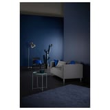 Modern living room with grey KLIPPAN sofa, blue cushions, side table, lamp, and cactus. Dark blue walls, carpet, and dramatic lighting.