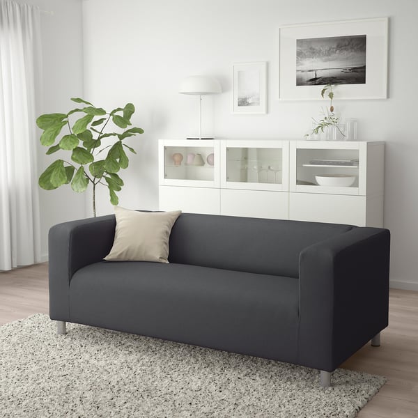 Modern living room with gray KLIPPAN sofa, white cabinet, green plant & rug.