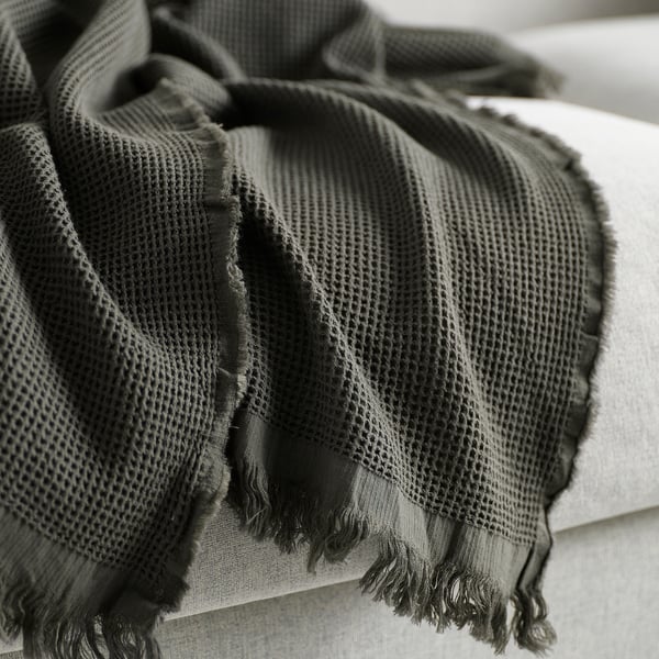 A cozy, folded black and grey striped throw blanket with fringes, showcasing its soft texture and quality craftsmanship.
