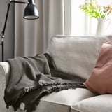 Grey throw blanket on light grey couch, red cushion, black lamp, flowers.