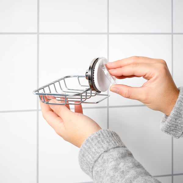 Person installs KROKFJORDEN soap dish, silver, on tiled wall using suction cup.
