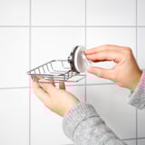 Person installs KROKFJORDEN soap dish, silver, on tiled wall using suction cup.