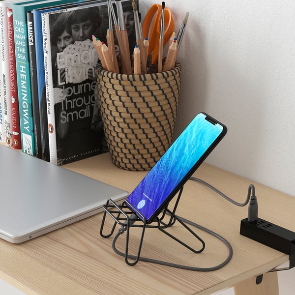 KRUBBET black mobile holder on desk, phone charging, near laptop, books, and pen cup.