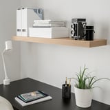Modern desk with LACK white wall shelf holding books, camera, and plant. BLACK desk with lamp, notebook, and pen holder.