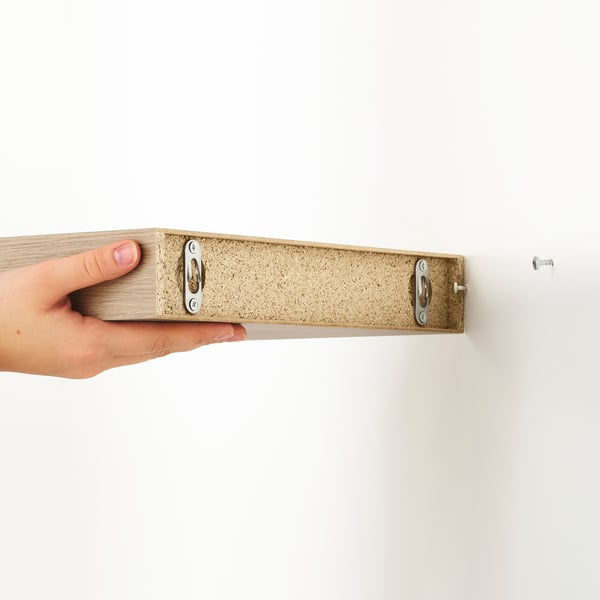 Hand holding LACK wall shelf by edge, showing hidden mounting brackets and minimalist design.