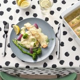 A meal of salmon, vegetables, and sauce on a plate with cutlery on a black and white polka dot tablecloth.