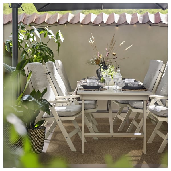 Outdoor dining setup with beige LÄTTBETONG rug, light wood table, and chairs with cushions.