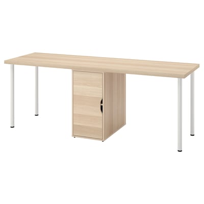 An LAGKAPTEN desk in light oak color with a storage cabinet. It a wooden top and white metal legs. The cabinet has a single door for storage.