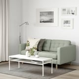 Modern living room with green 2-seat sofa, white coffee table, lamp, and striped rug.