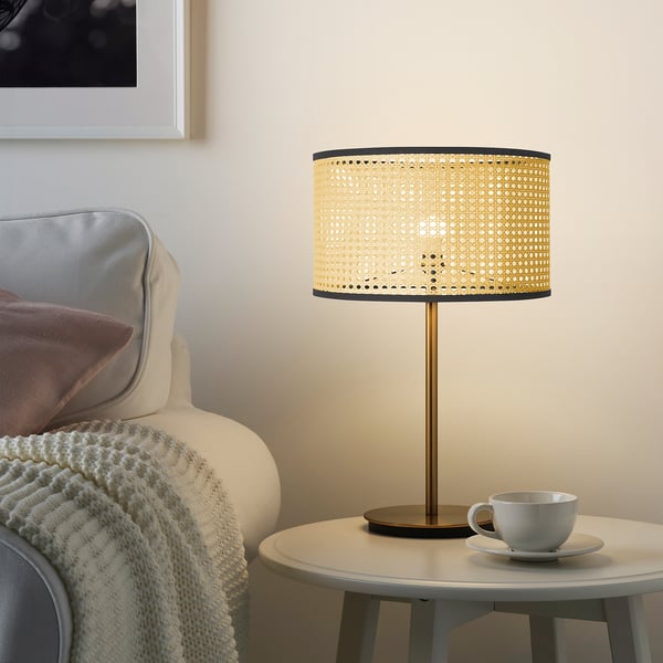 LÅNGSKEPPS lamp on table, warm glowing light, natural rattan texture, conical shape, cozy living room scene.