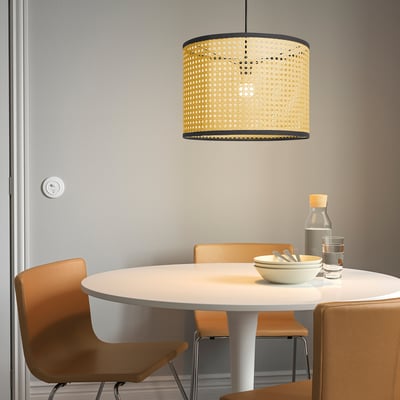 A large LÅNGSKEPPS lamp hangs over a small round dining table with wooden chairs, casting warm light. The table holds a bowl, glass, and bottle.