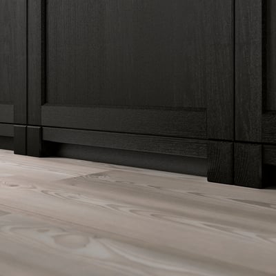 A close-up of black wooden kitchen cabinets with beveled edges on a light wooden floor. The functional base area of the cabinets.