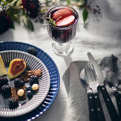 A dining setup with blue plate, black cutlery, and glass of drink.