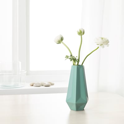 Geometric teal vase holding white flowers on a table. Bright, minimalist decor.