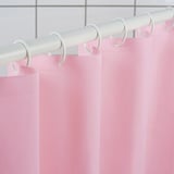 Light pink shower curtain hangs from white rod with rings, creating a harmonious and clean look in the bathroom.