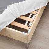 Wooden bed frame with visible slats, part of LYNGÖR base, holding white mattress and bedding.