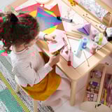A child crafts with colorful paper and paint at a wooden table.