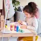 Girl painting at table with colors, in grey sweater and yellow pants.