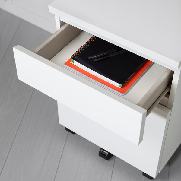 White MALM drawer unit on wheels with notebook and pens inside, ready for use.