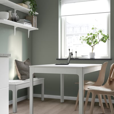 Cozy workspace with desk, laptop, plant, candle, chair, green walls, bookshelf.
