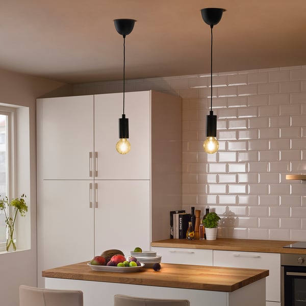 Modern kitchen with white cabinets, wooden counter, and two black pendant lights illuminating a bowl of fruit.
