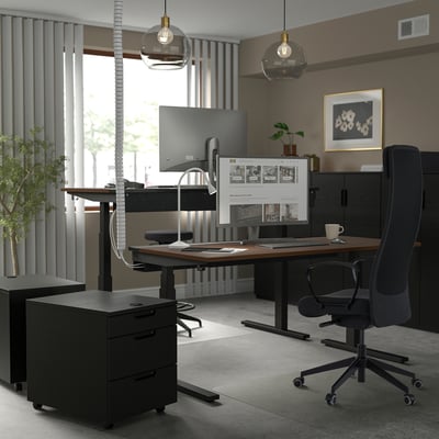 Home office with ergonomic chair, desk, dual monitors, lights, plant, and art.