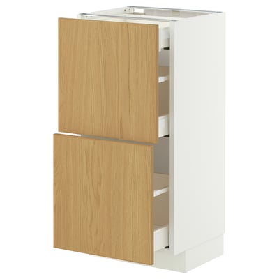 An IKEA METOD kitchen cabinet with light wooden doors and white sides. It includes multiple drawers and has a modern design.