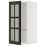 A white METOD wall cabinet with black bodbyn glass doors featuring beveled edges. The cabinet has an adjustable shelf and sturdy construction.
