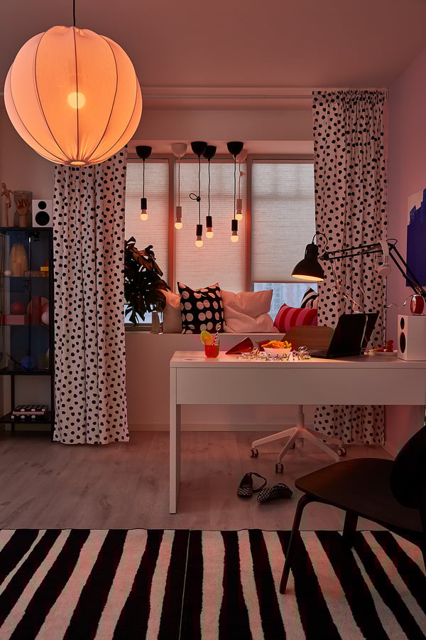Modern home office MICKE white desk, zebra rug, polka dot curtains, pendant lights, pink walls, and black lamp.