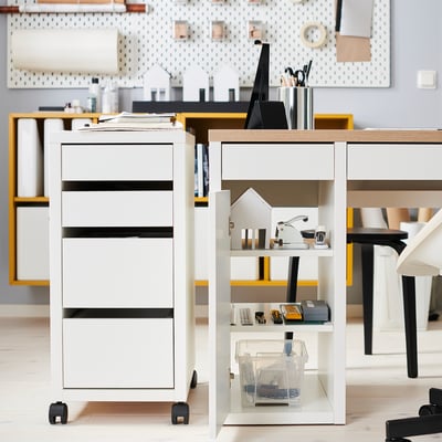 Modern white desk with drawers and shelves, featuring neatly arranged supplies and a house-shaped decoration.