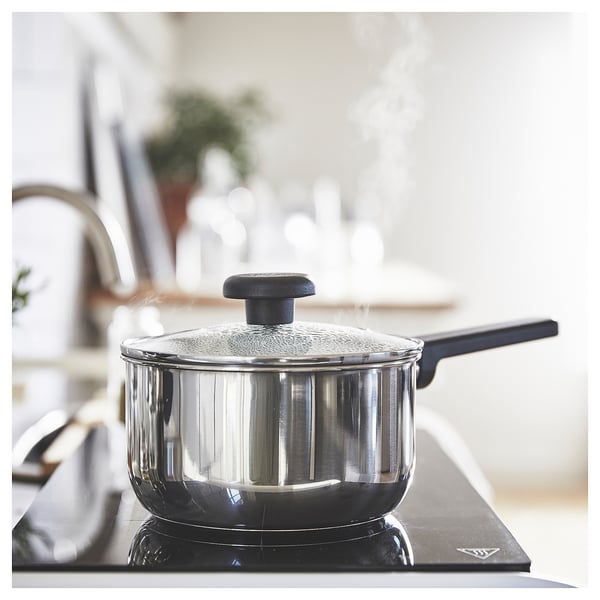 Modern kitchen with MIDDAGSMAT saucepan on stove. Silver, rounded with black handle and lid. Cooking over electric burner.