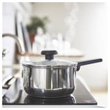 Modern kitchen with MIDDAGSMAT saucepan on stove. Silver, rounded with black handle and lid. Cooking over electric burner.